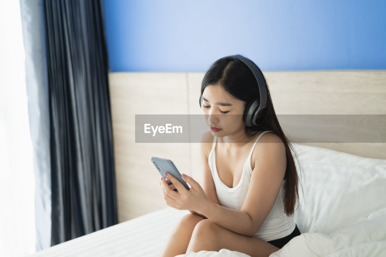 Young woman using mobile phone while sitting on bed