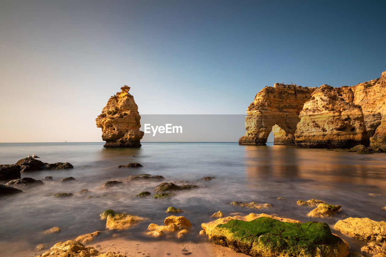 Rock formations on beach against clear sky