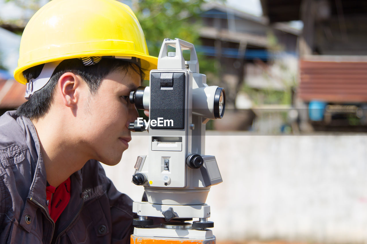 Side view of engineer looking through theodolite at construction site