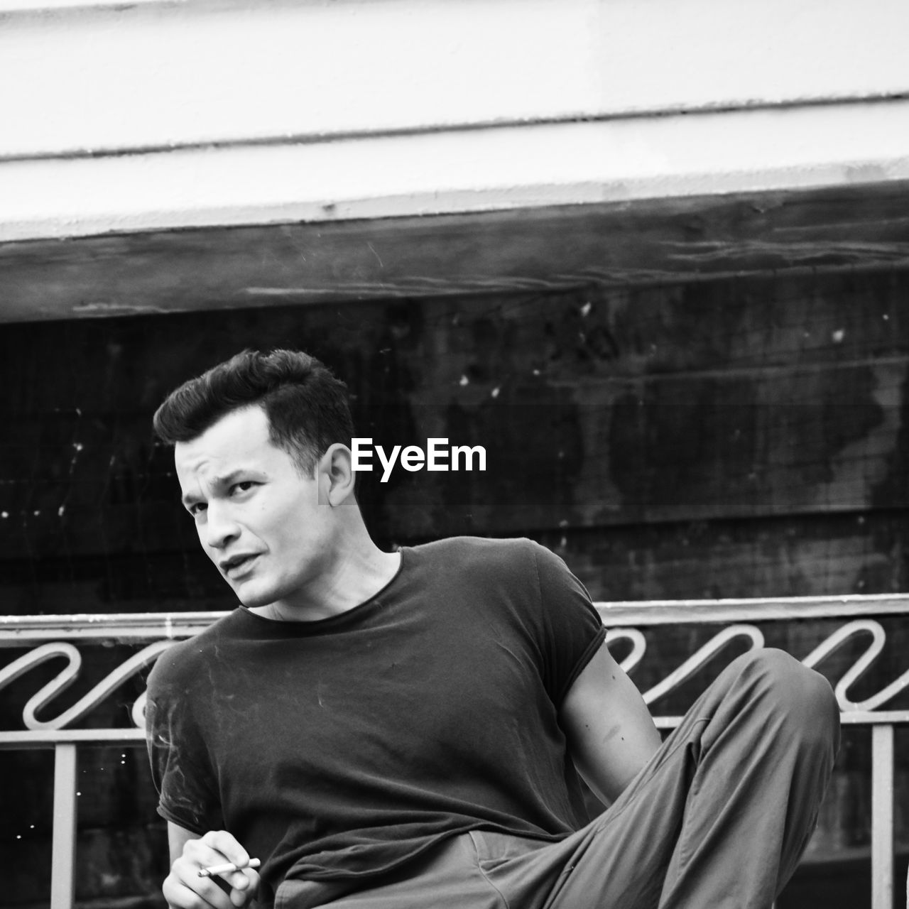 Portrait of young man looking away while sitting on window