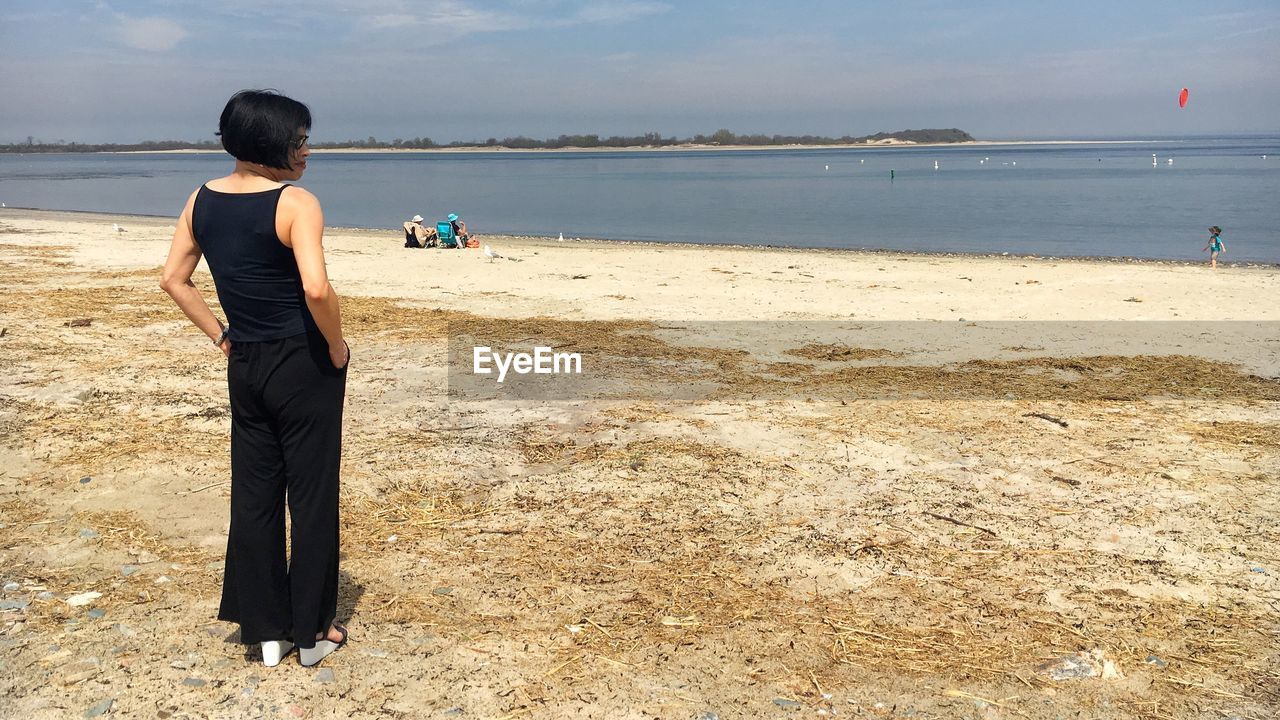 Rear view of woman standing at beach during sunny day