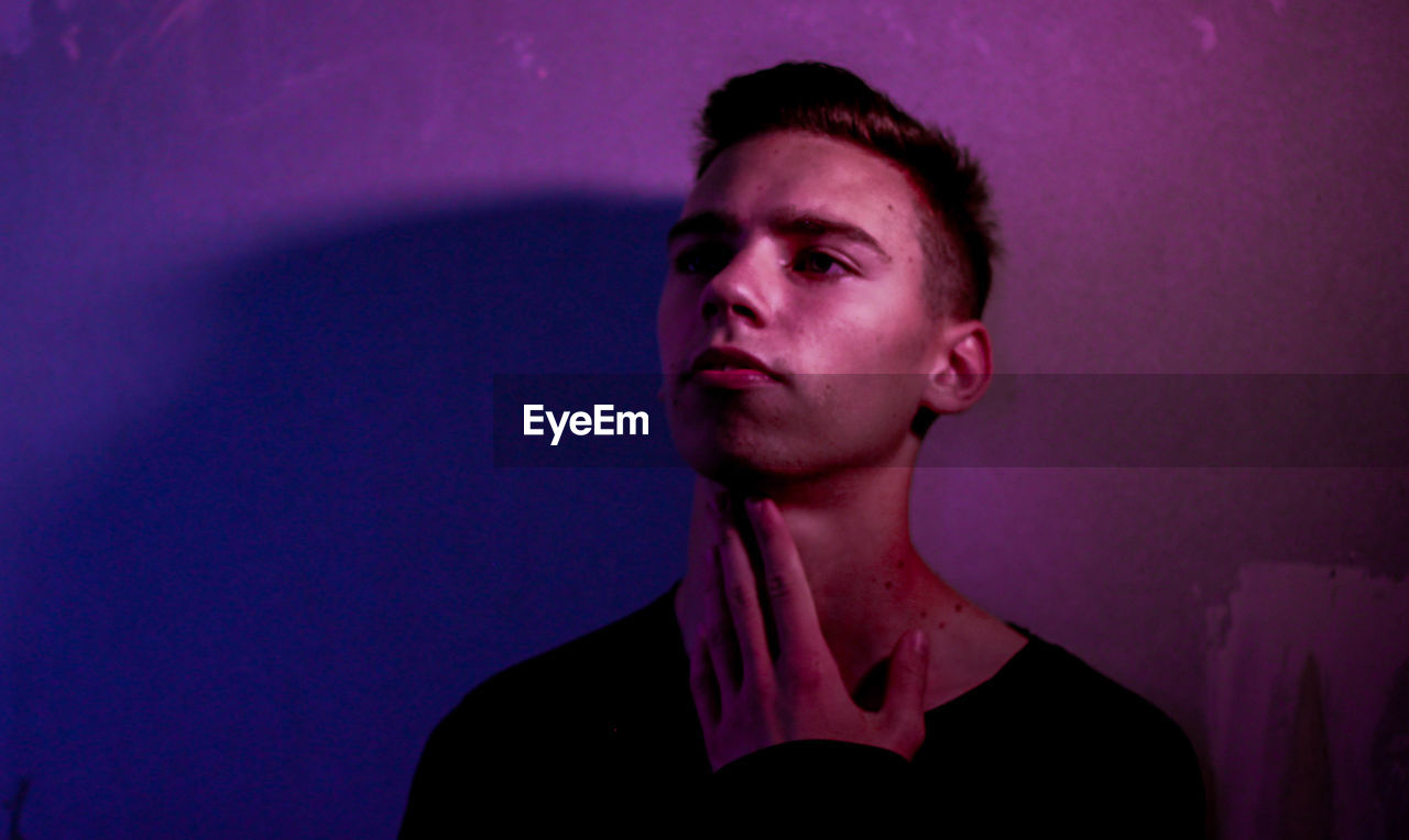 PORTRAIT OF YOUNG MAN LOOKING AWAY AGAINST GRAY BACKGROUND