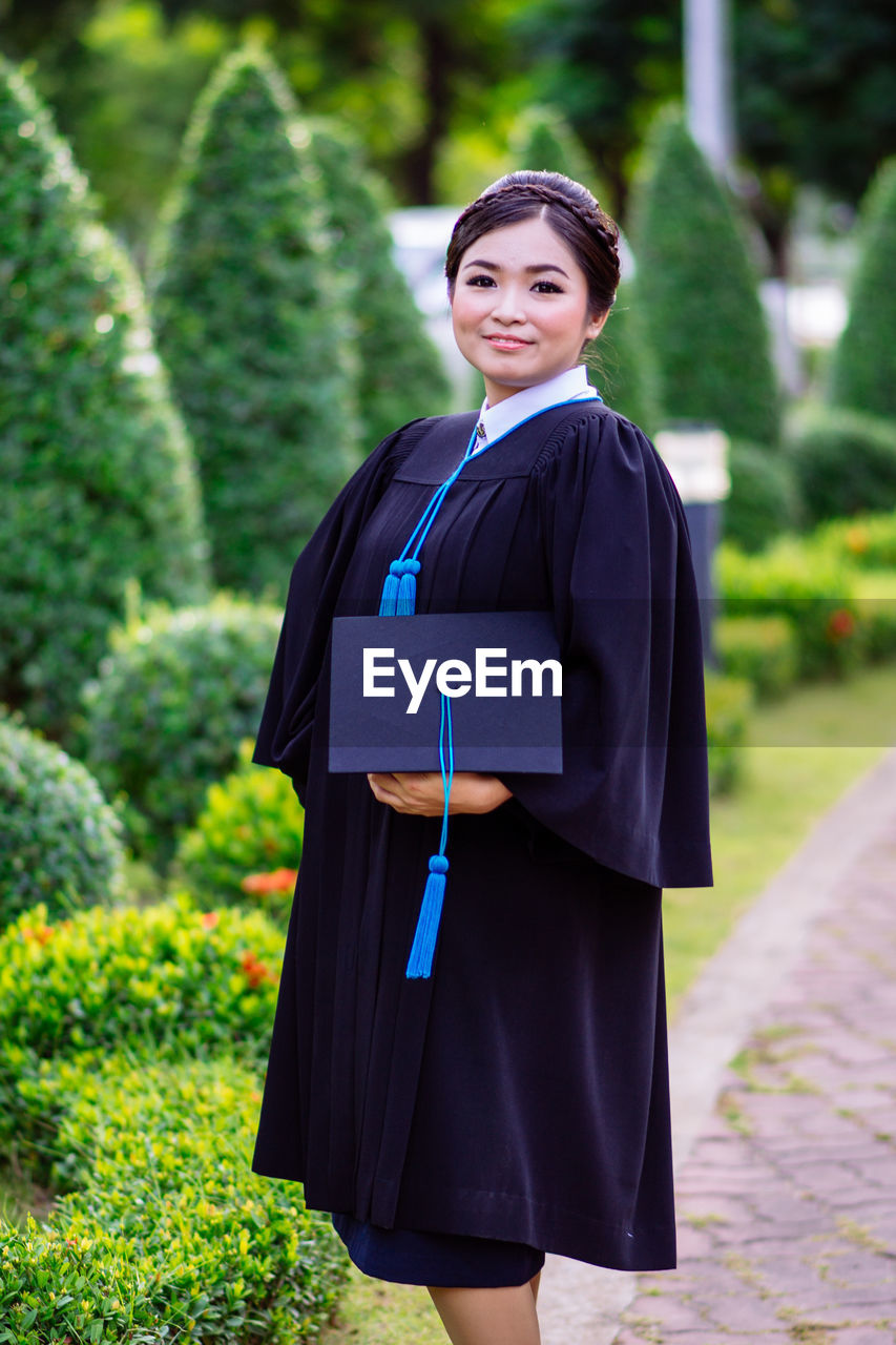 Portrait of smiling young woman wearing graduation gown standing outdoors