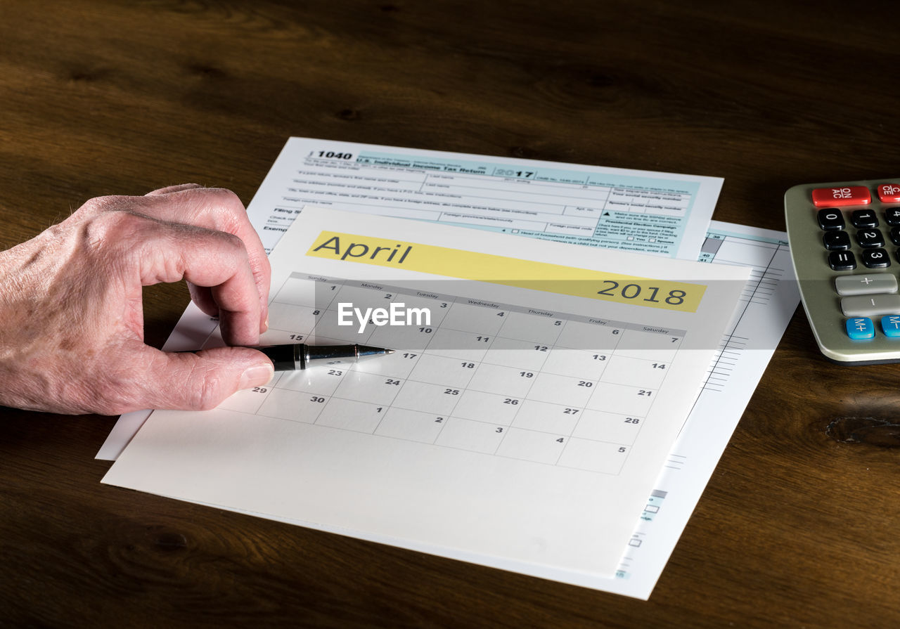 Cropped hand of senior man with pen and calendar on table