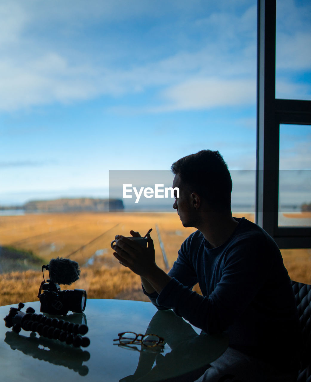 Side view of young man looking through window while sitting in restaurant