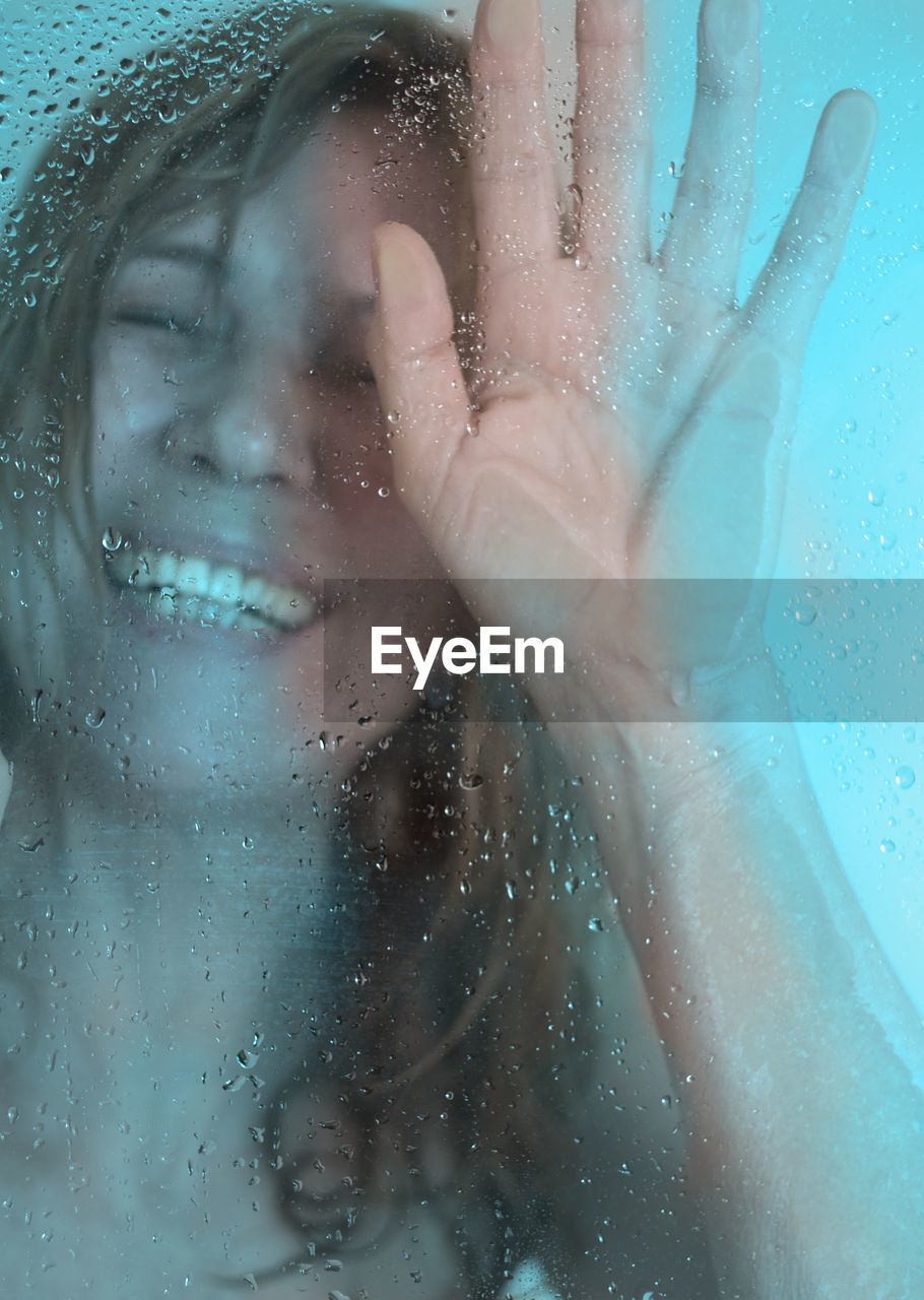 Close-up of smiling woman taking shower seen through glass