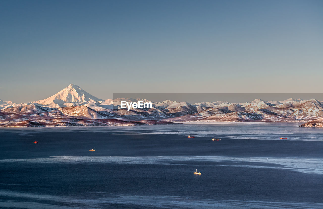 Scenic view of sea amidst snowcapped mountains against clear sky