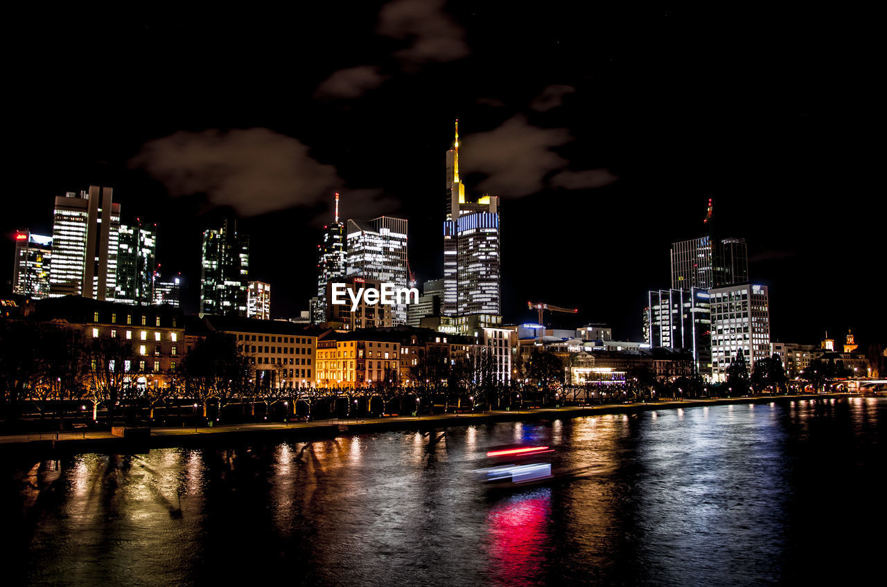 Illuminated buildings by river against sky at night