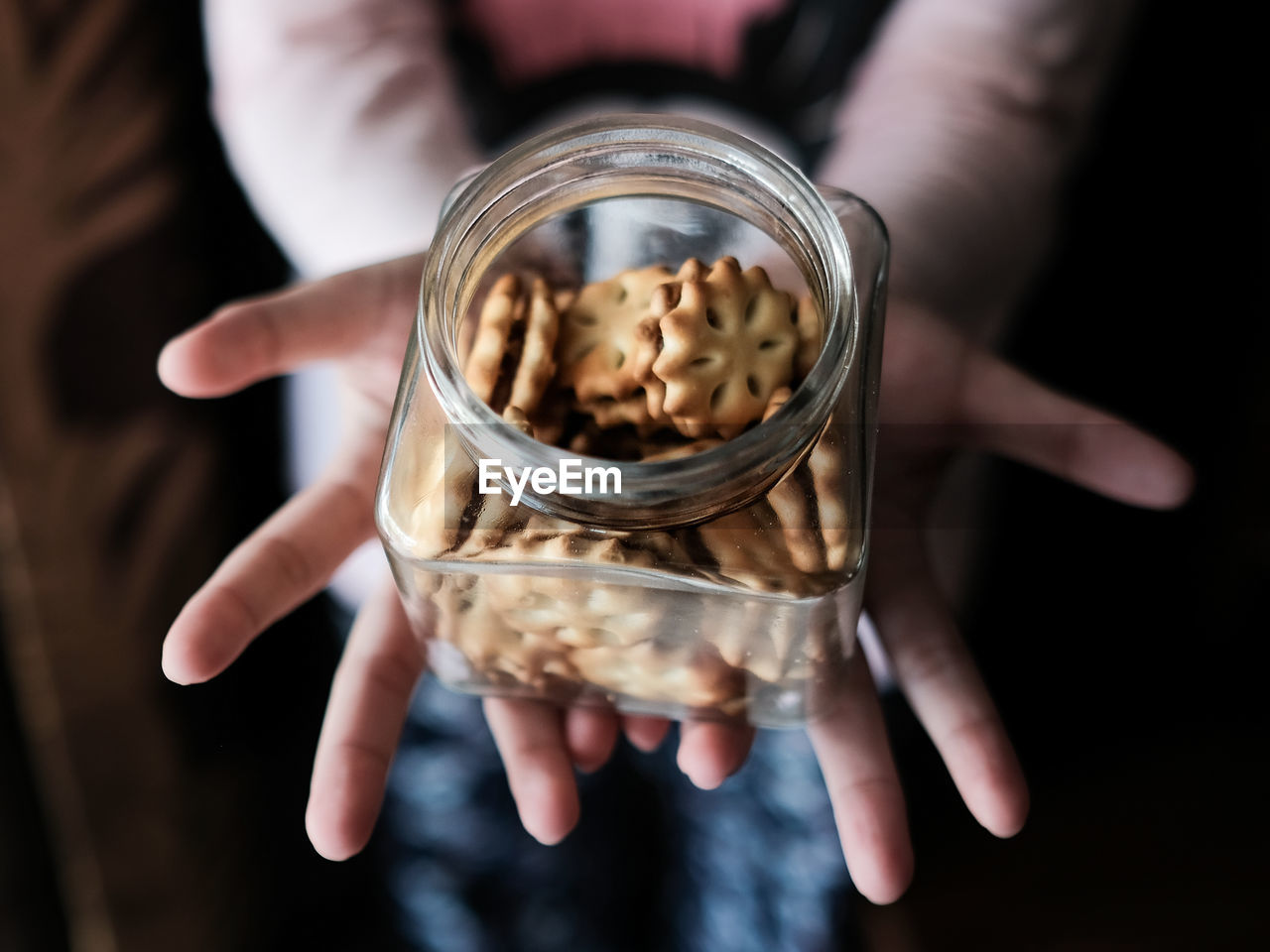 Close-up of a woman holding cookies in a glass jar