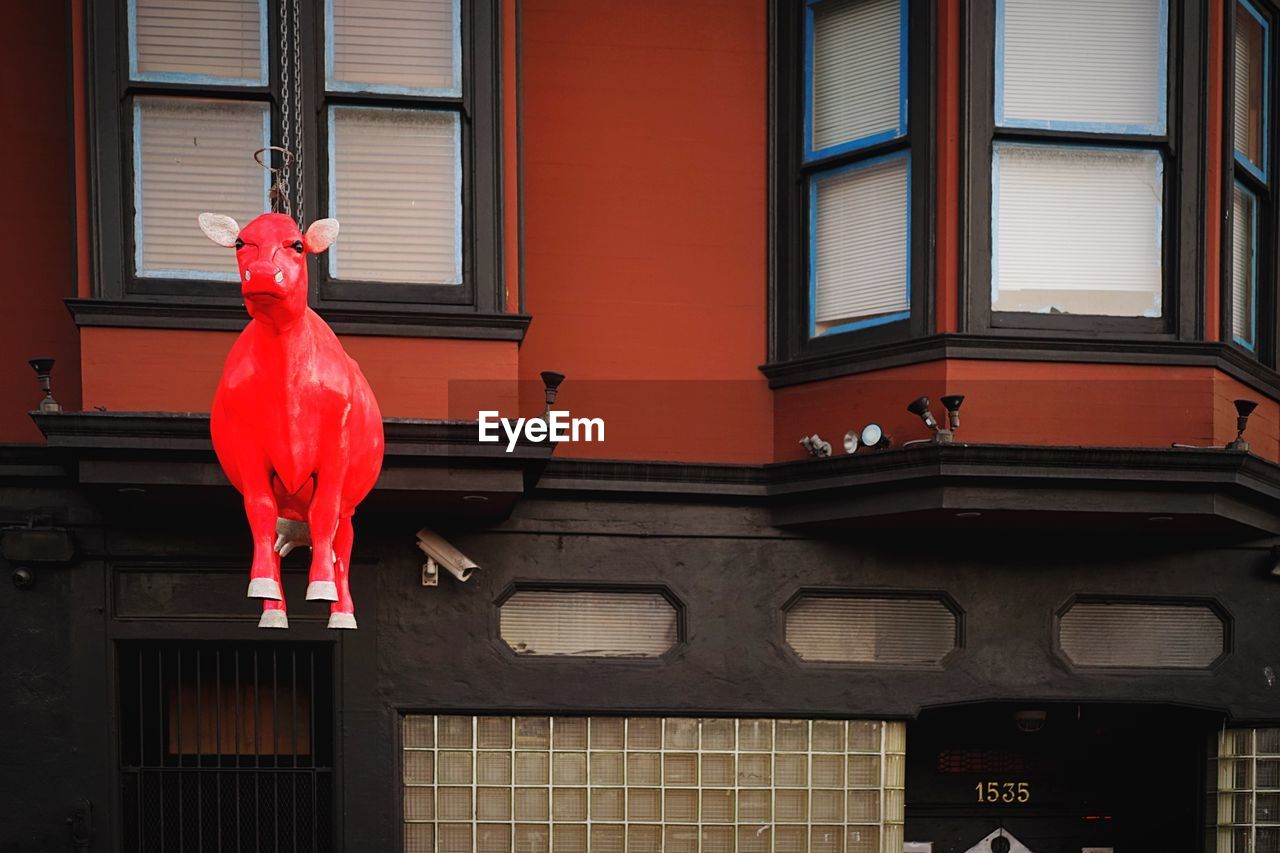 Low angle view of red animal statue hanging against building in city