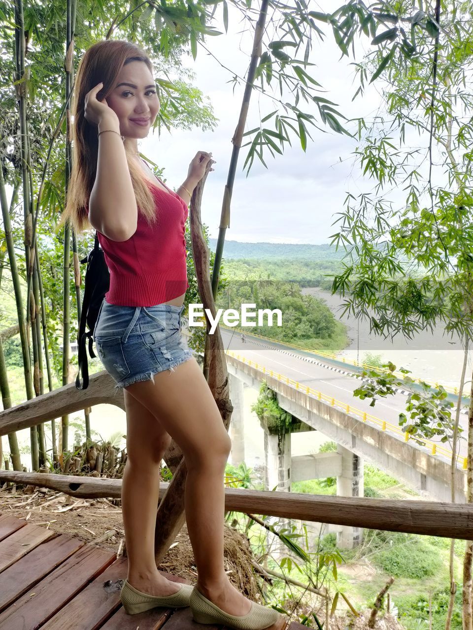 YOUNG WOMAN STANDING BY RAILING AGAINST TREE