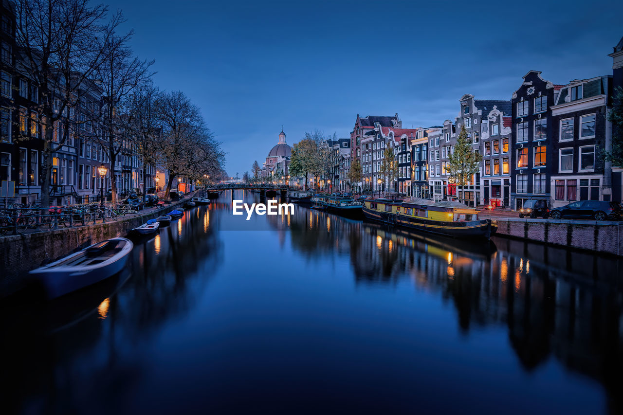 Canal amidst illuminated city buildings against sky at dusk