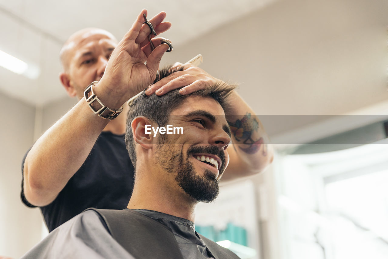 Low angle view of barber cutting man hair in salon