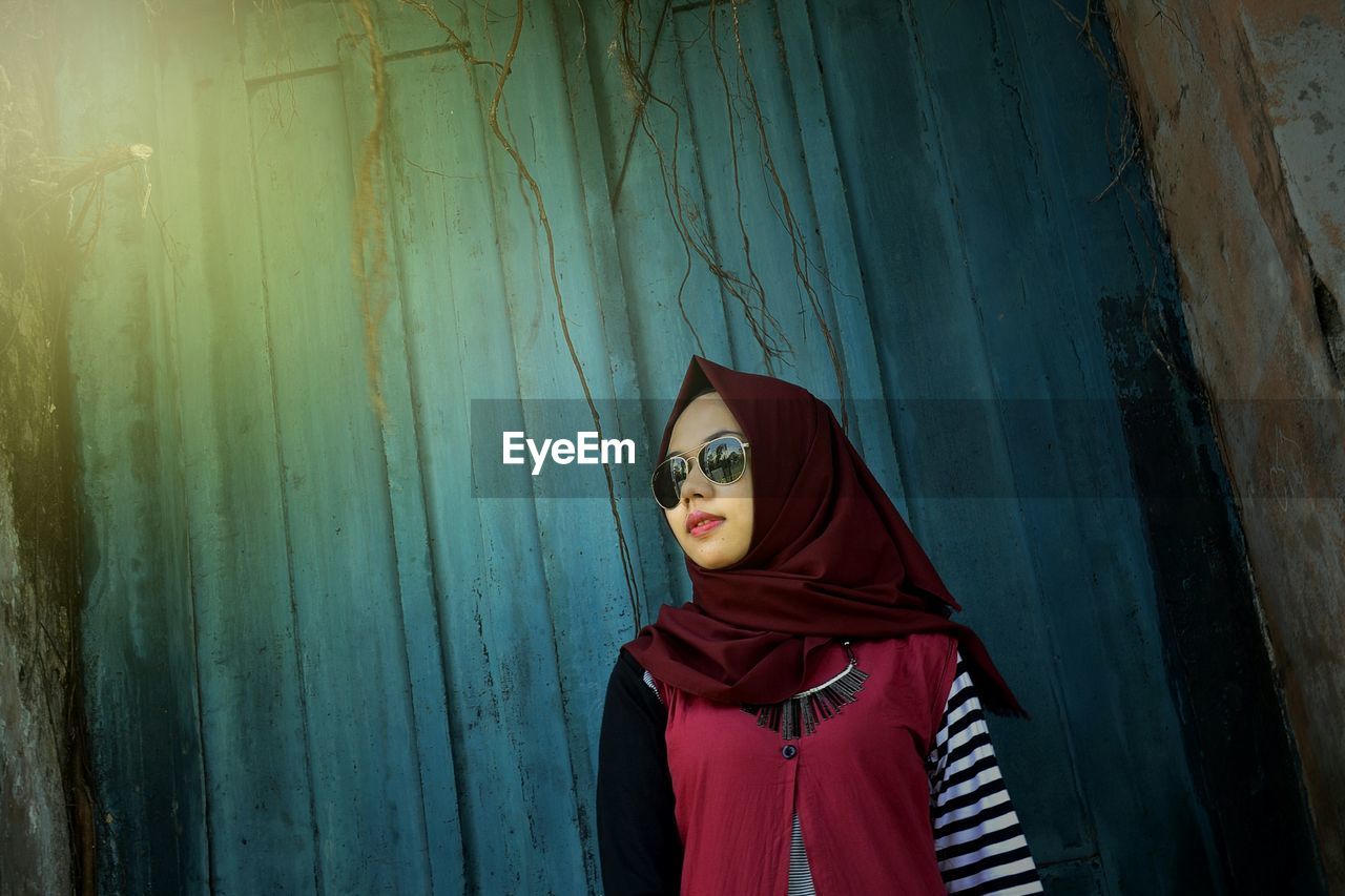 Low angle view of woman in sunglasses standing against wall