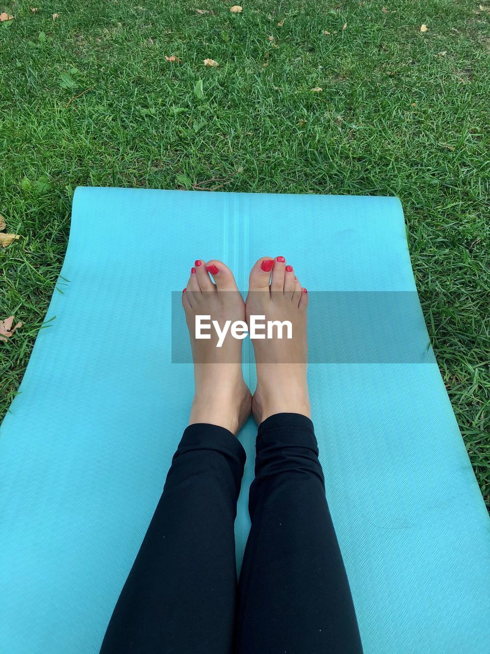 Low section of woman relaxing on exercise mat in park