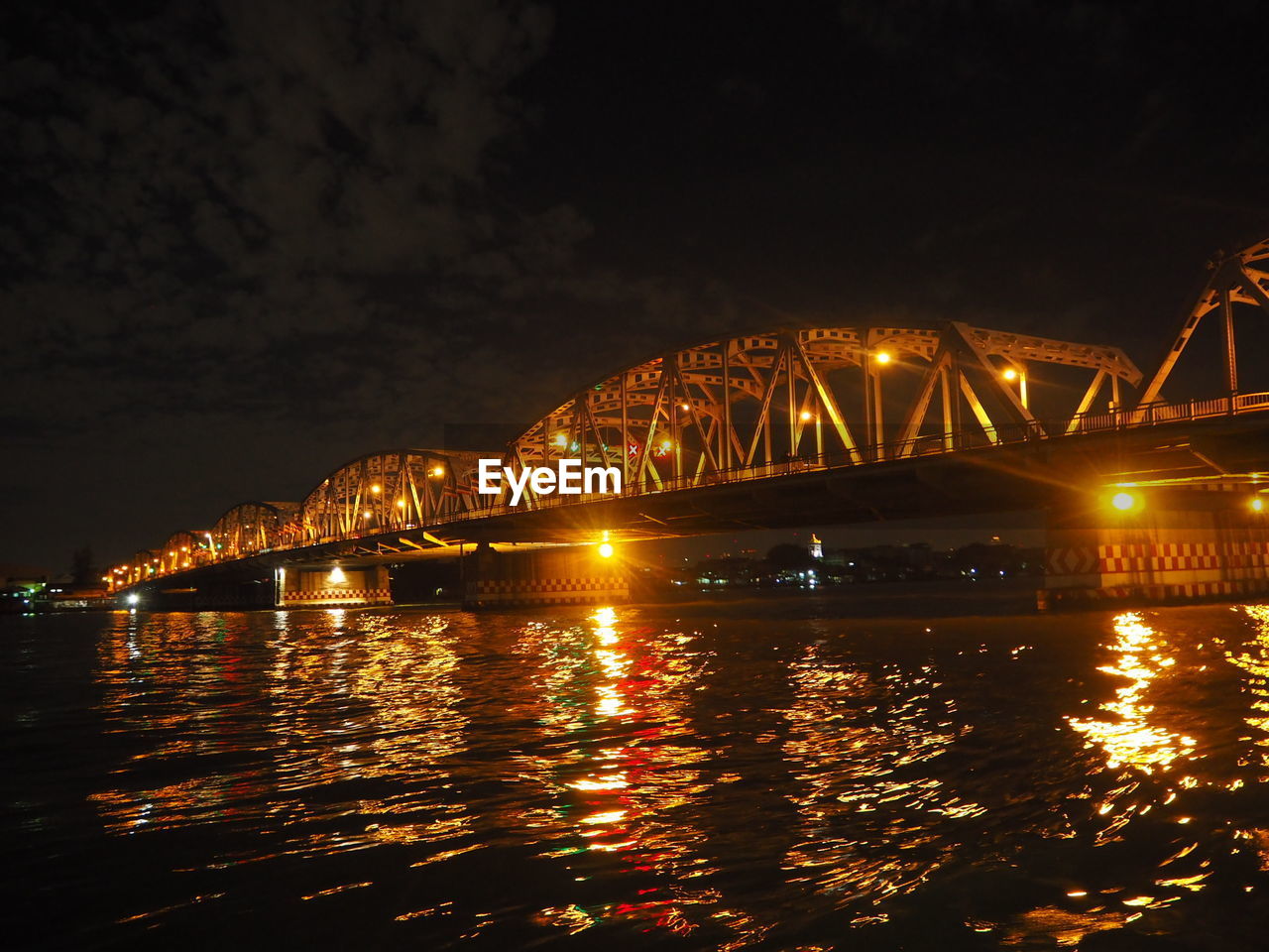 ILLUMINATED BRIDGE OVER RIVER AGAINST SKY AT NIGHT