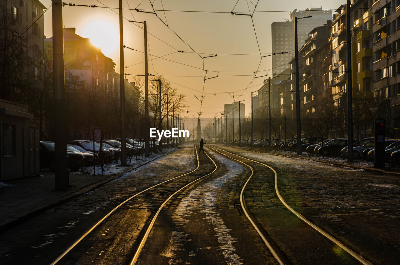 View of railway tracks amidst city against sky during sunset