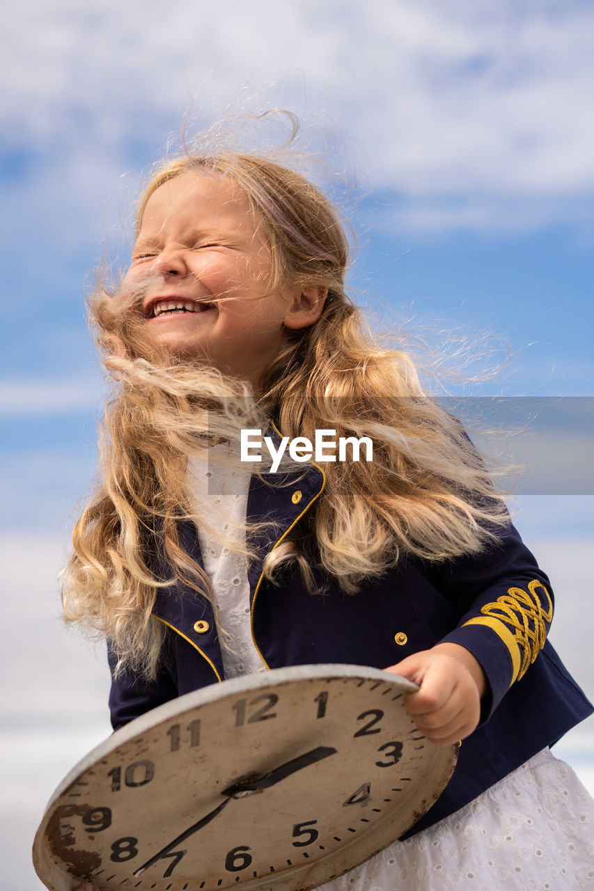 Child girl in jacket laughing and holding clock at the beach