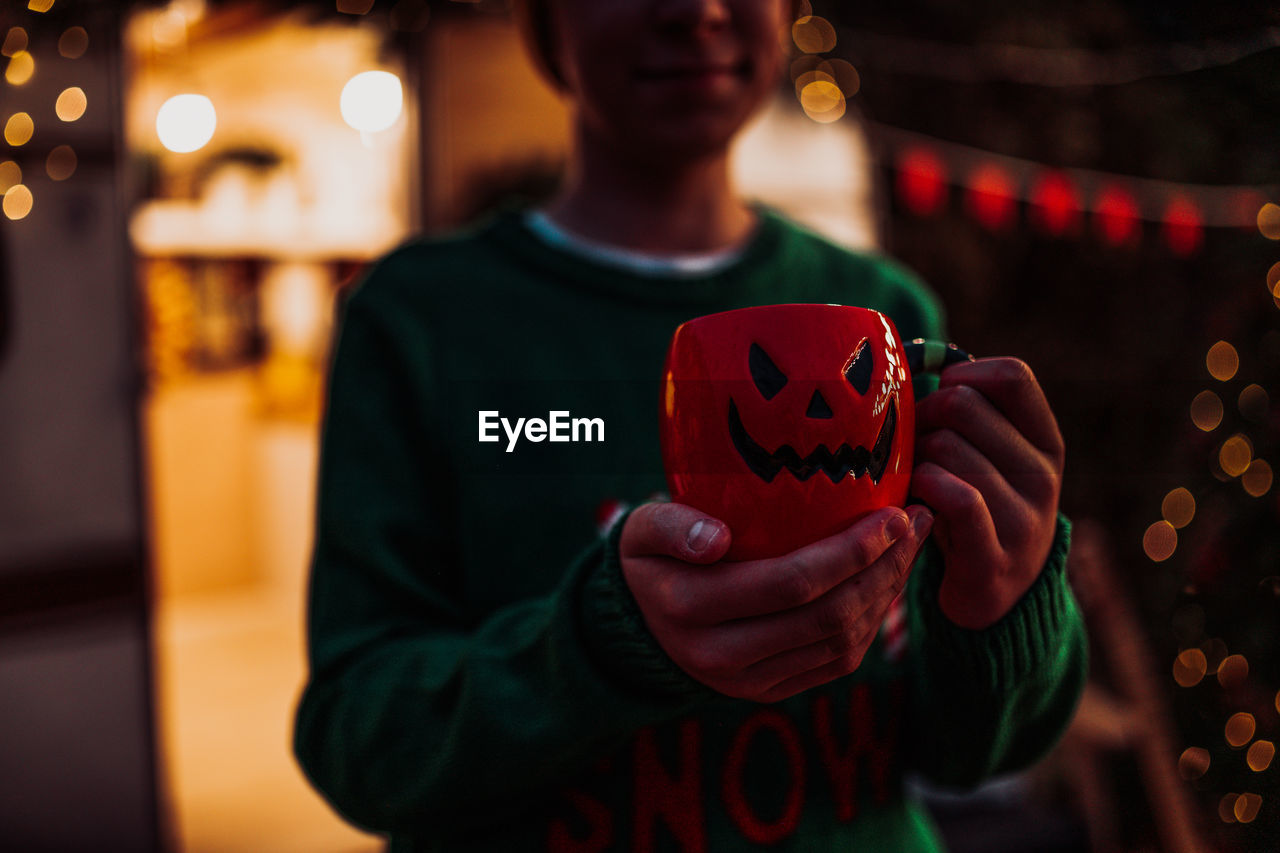 Midsection of boy holding jack o lantern cup at home