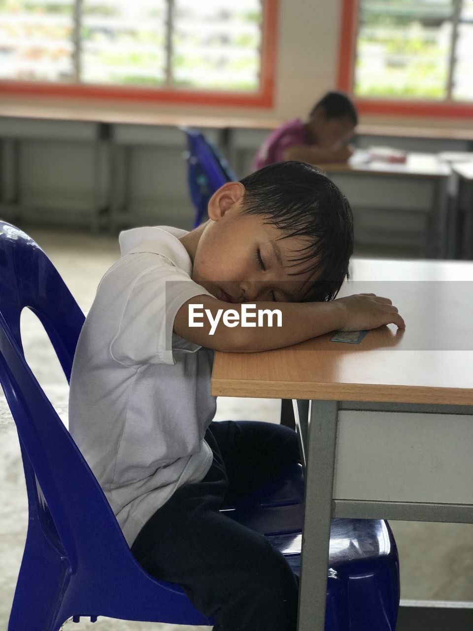 Side view of boy sitting on table while sleeping 