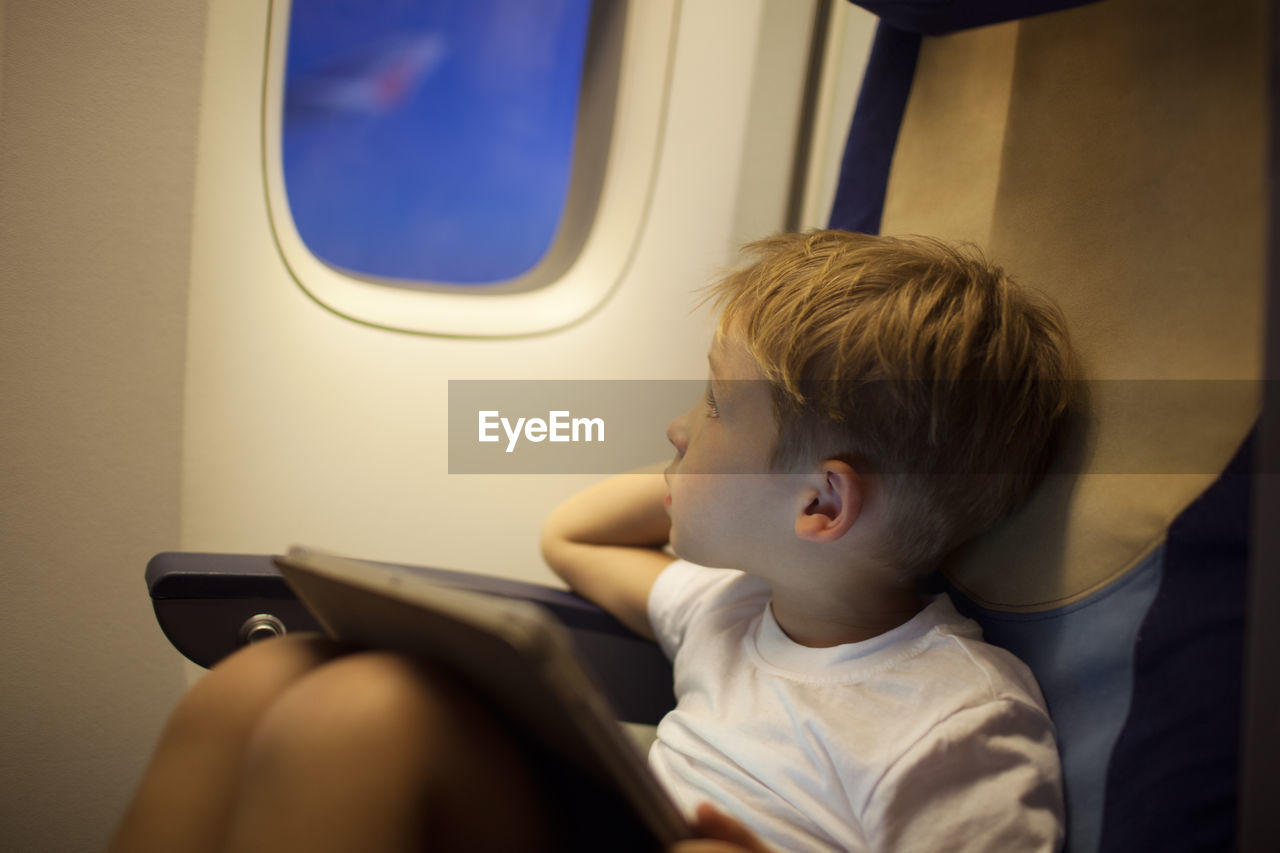 Boy looking away while sitting with digital tablet in airplane