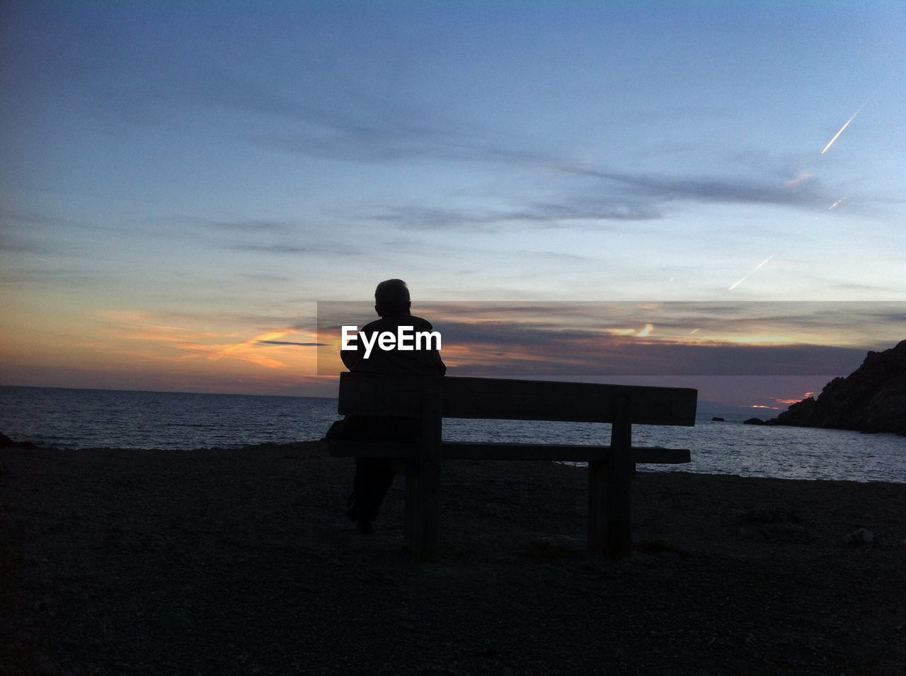 View of person sitting on bench at sunset