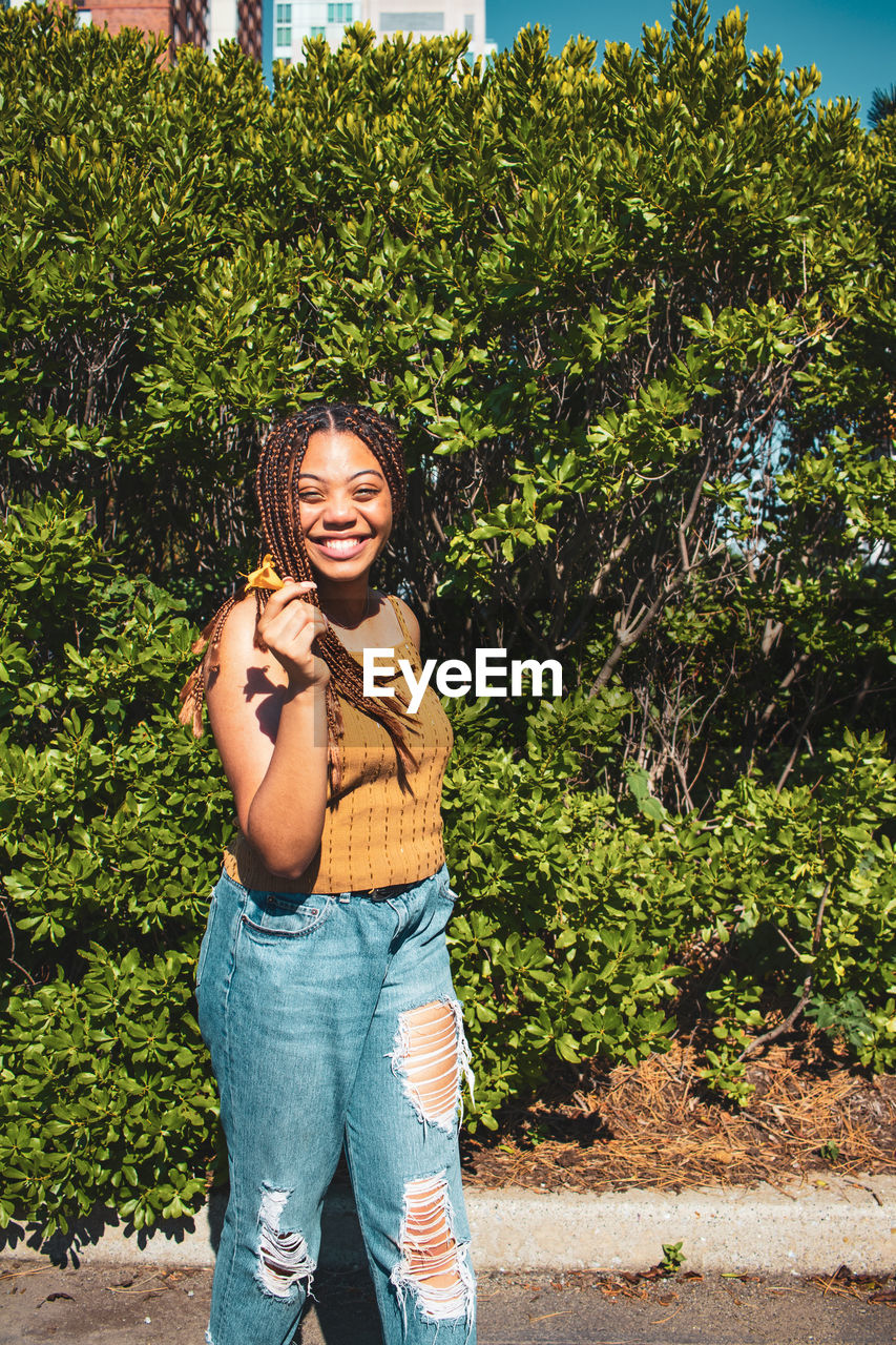 PORTRAIT OF SMILING GIRL STANDING AGAINST PLANTS