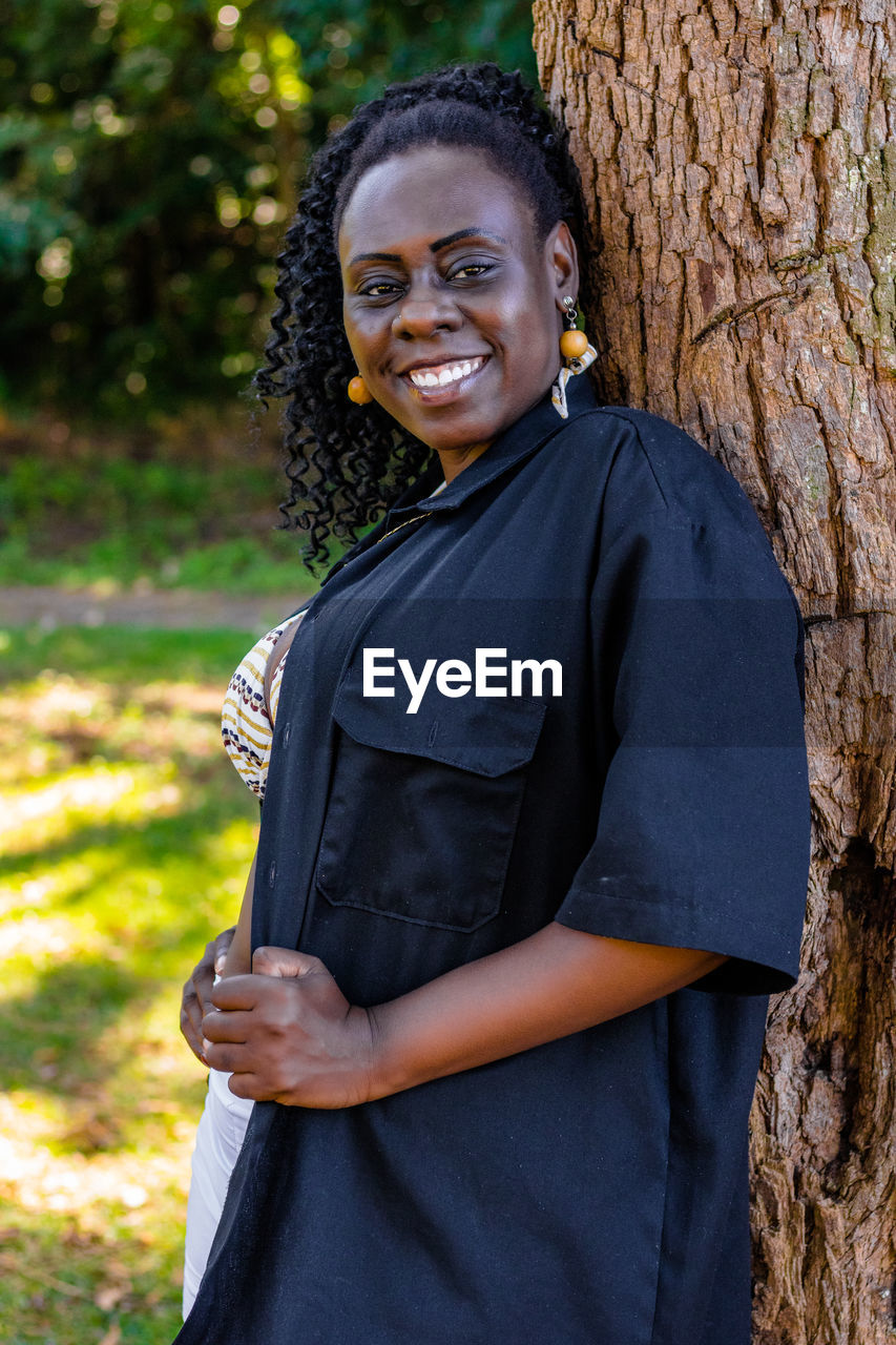 Portrait of smiling woman standing by tree trunk