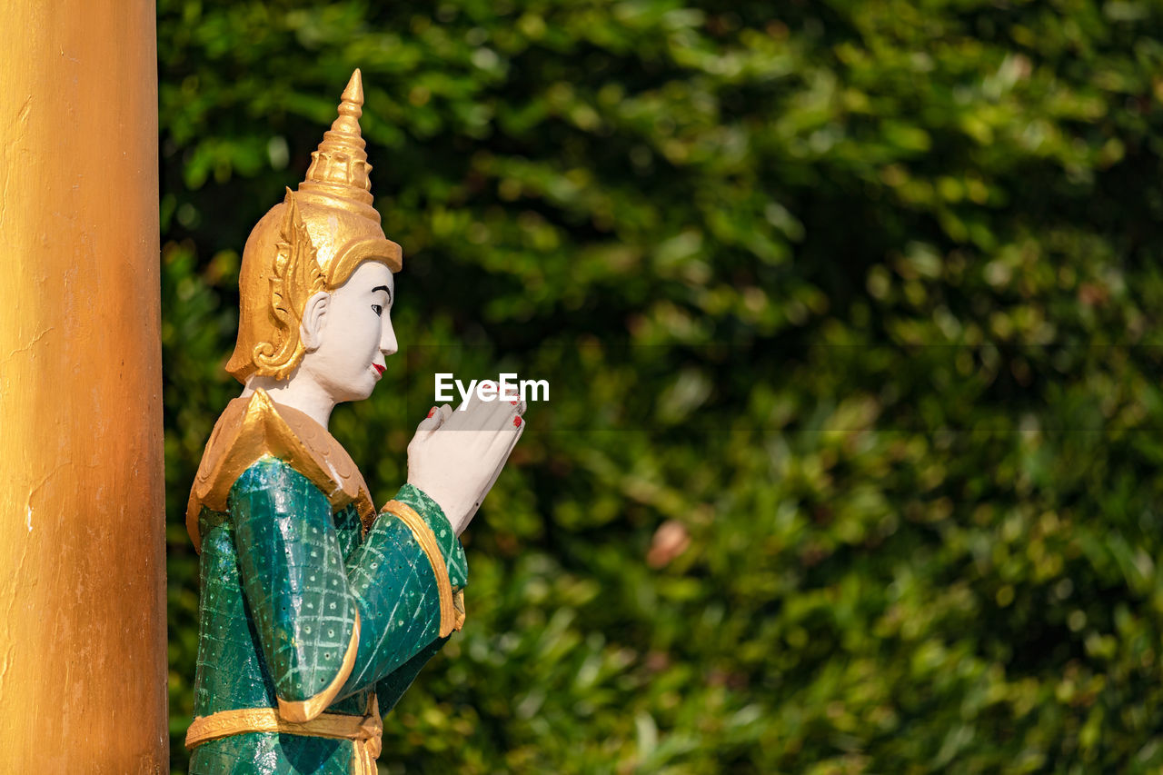 A praying buddha statue with folded hands in a temple against a natural background in myanmar