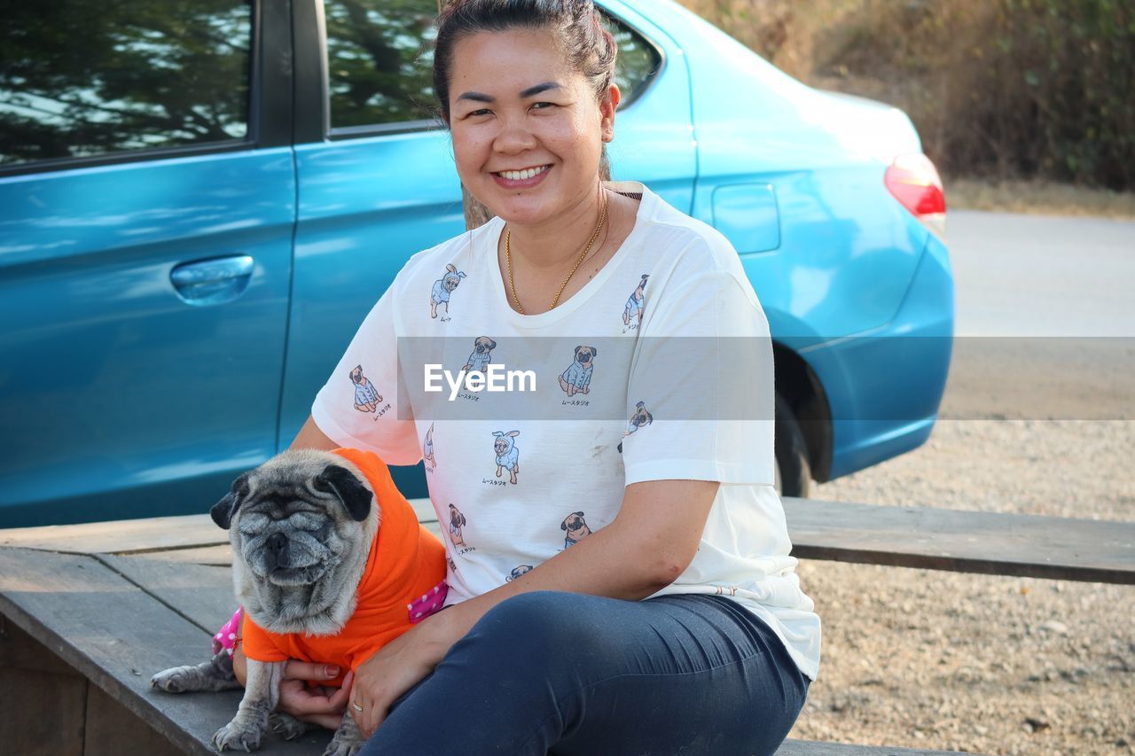 Portrait of smiling woman with dog by car