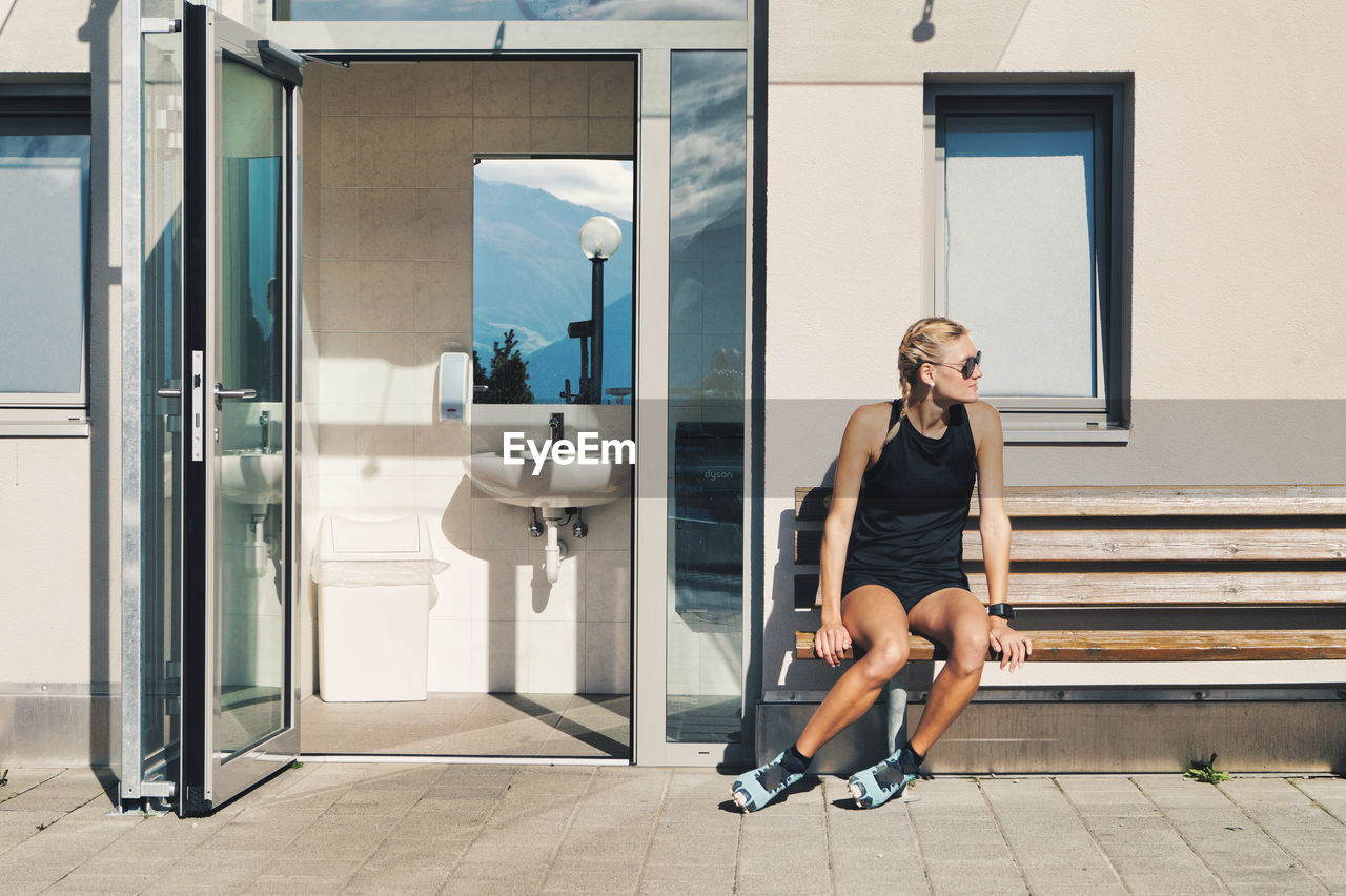 Woman sitting at entrance of cable car station building and open public toilet door, naturno