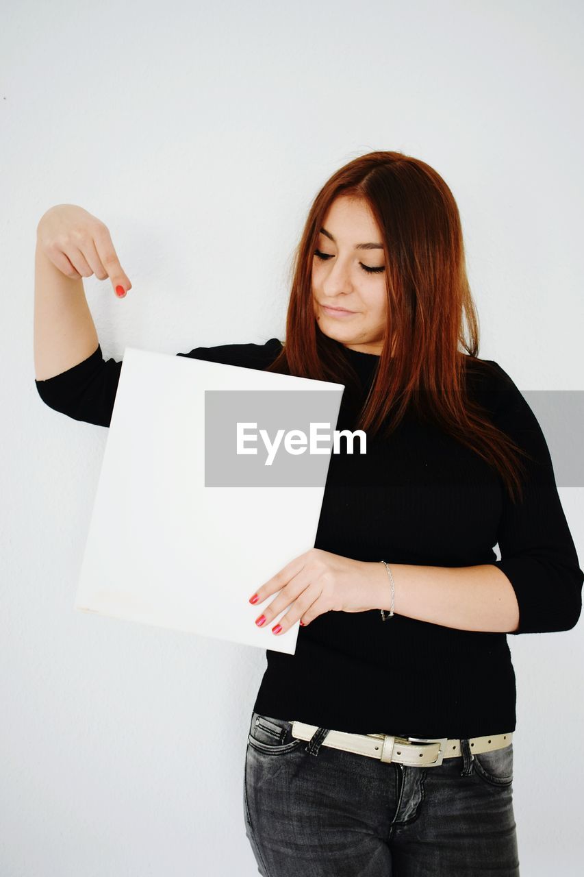 Young woman holding blank placard while standing against white background