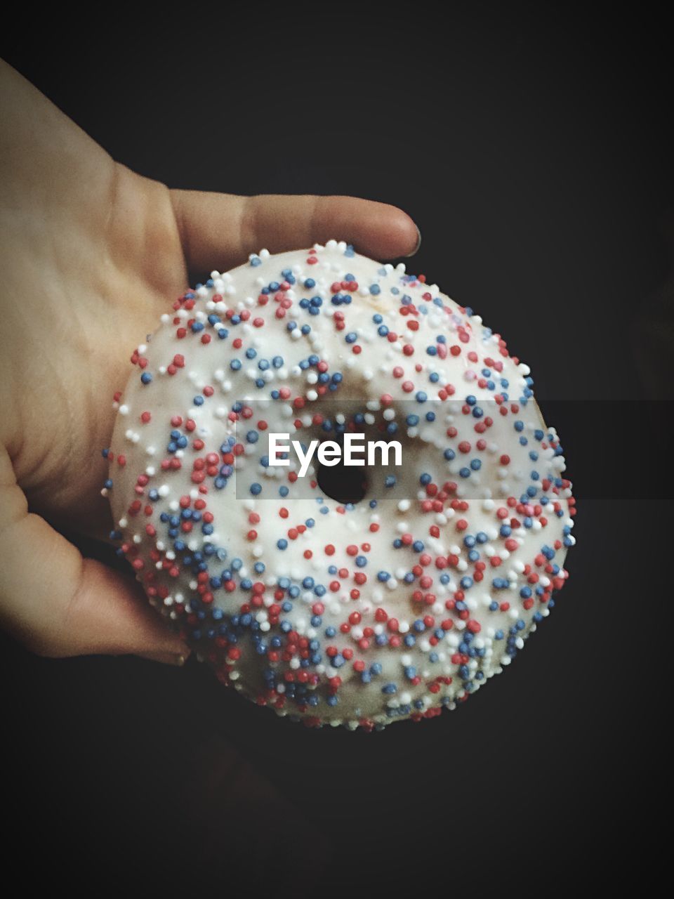 Cropped image of hand holding donut against black background