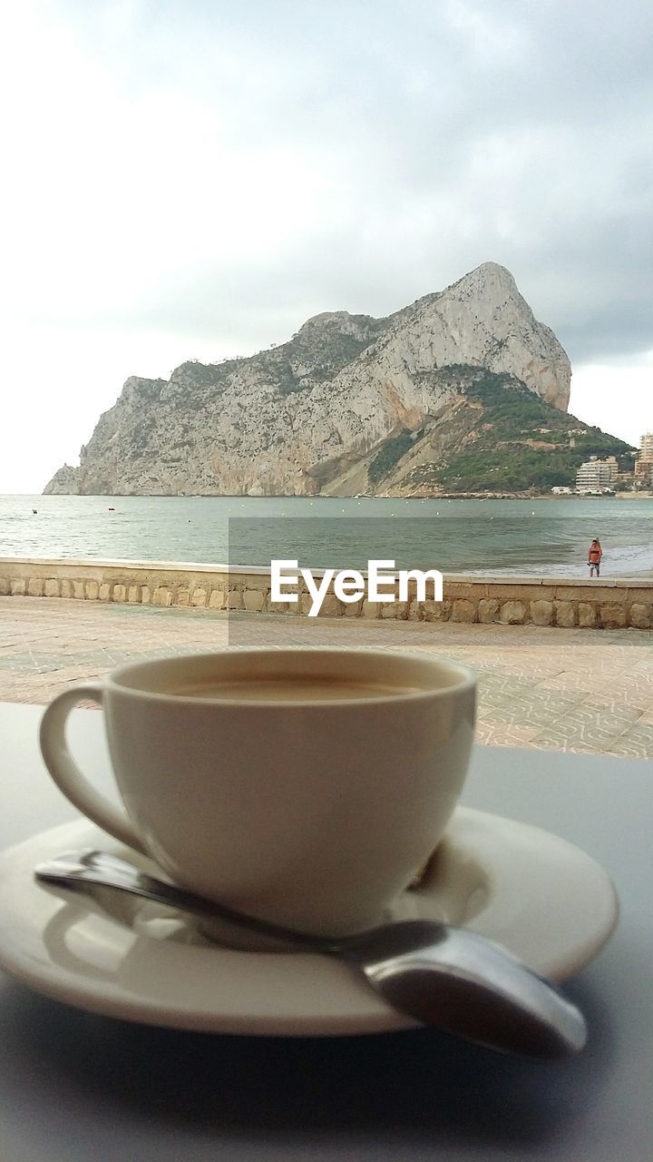 CLOSE-UP OF COFFEE ON TABLE AGAINST SEA