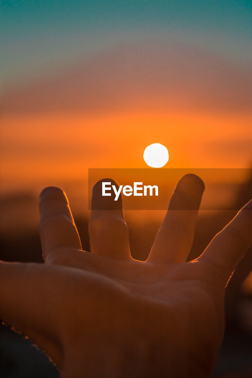 Close-up of hand against sun during sunset