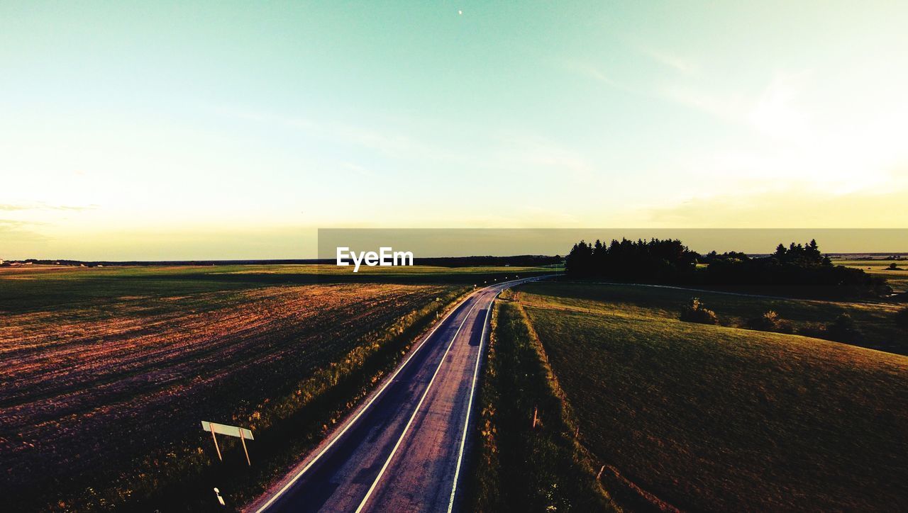 Road amidst field against sky during sunset