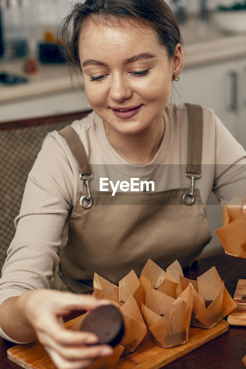 Young woman packs cupcakes in craft. concept of food delivery. business. bakery chef bakes pastrie 