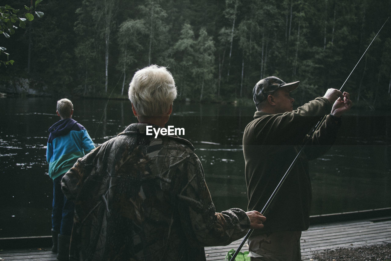 People fishing while standing at pier by lake