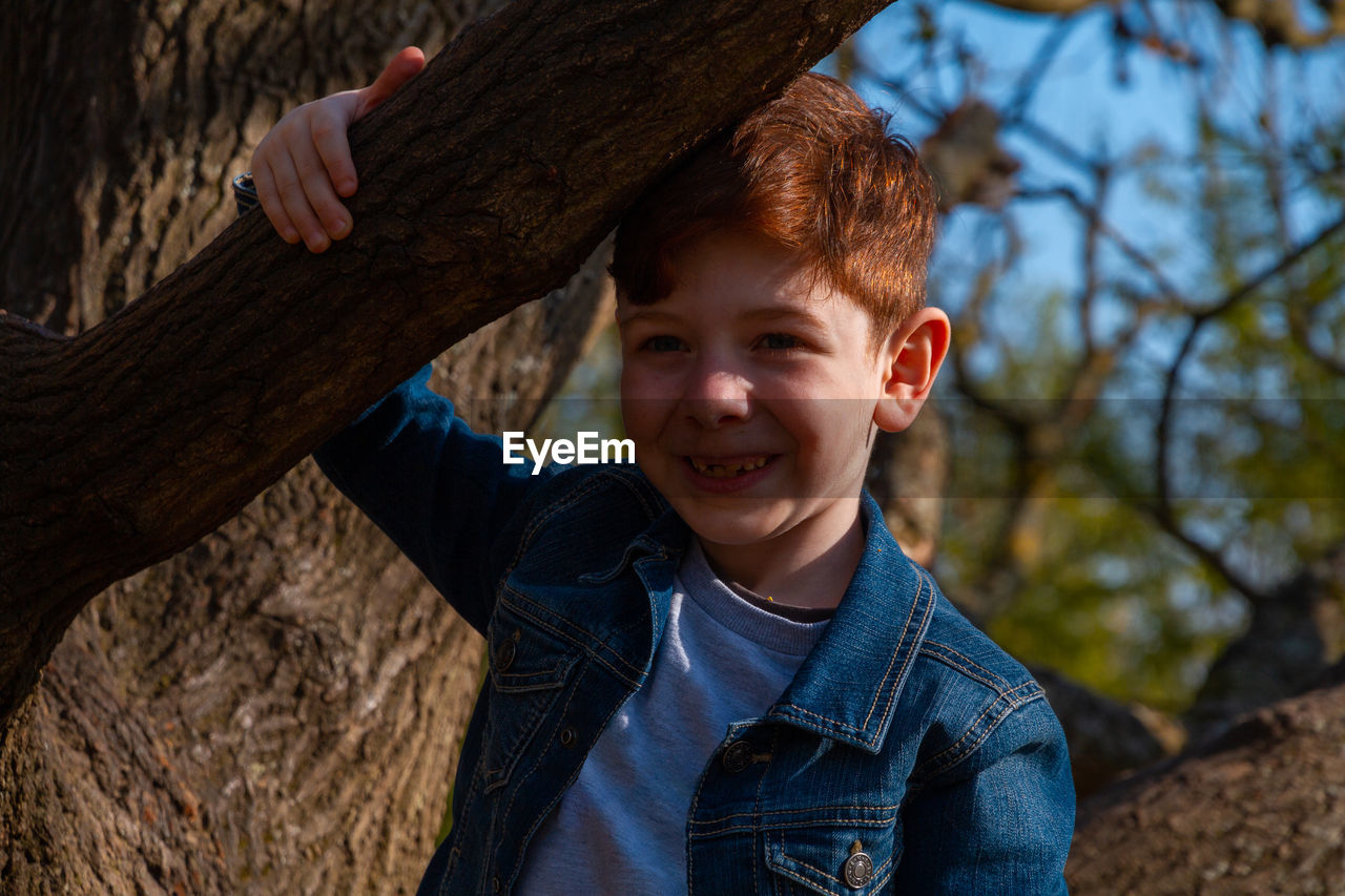 Portrait of boy smiling by tree trunk