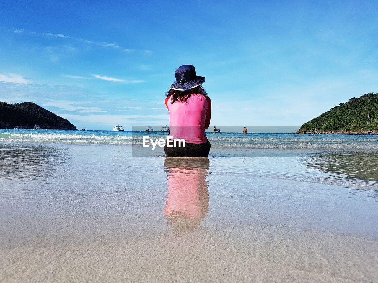 Rear view of mature woman sitting at beach against sky