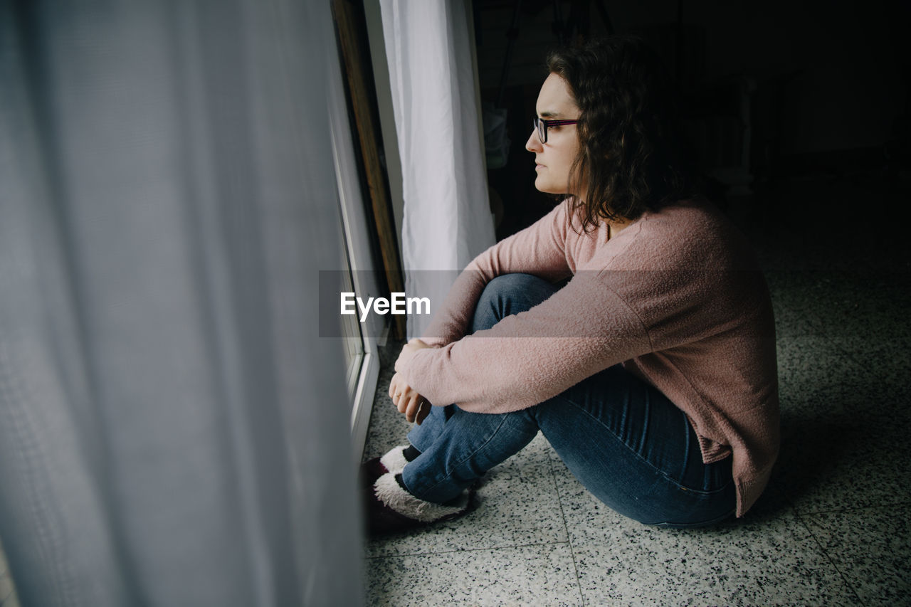 Woman with glasses sitting on the floor looking out the window