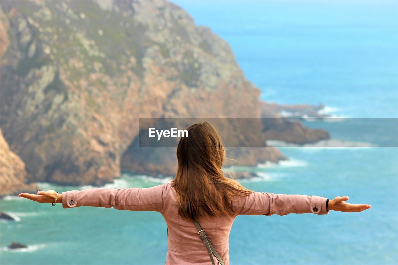 Rear view of woman with arms outstretched standing against sea