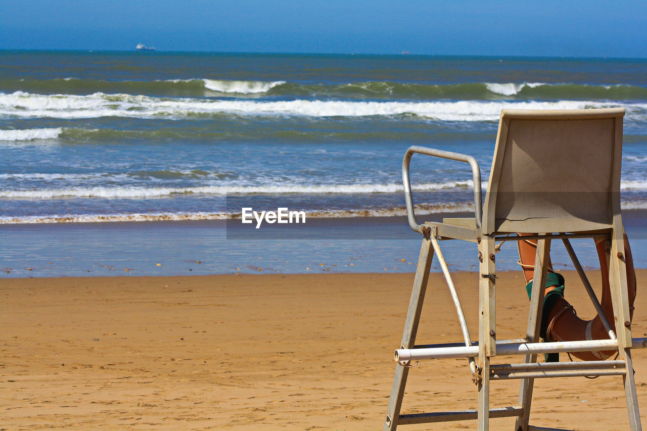 Chair on beach by sea against sky