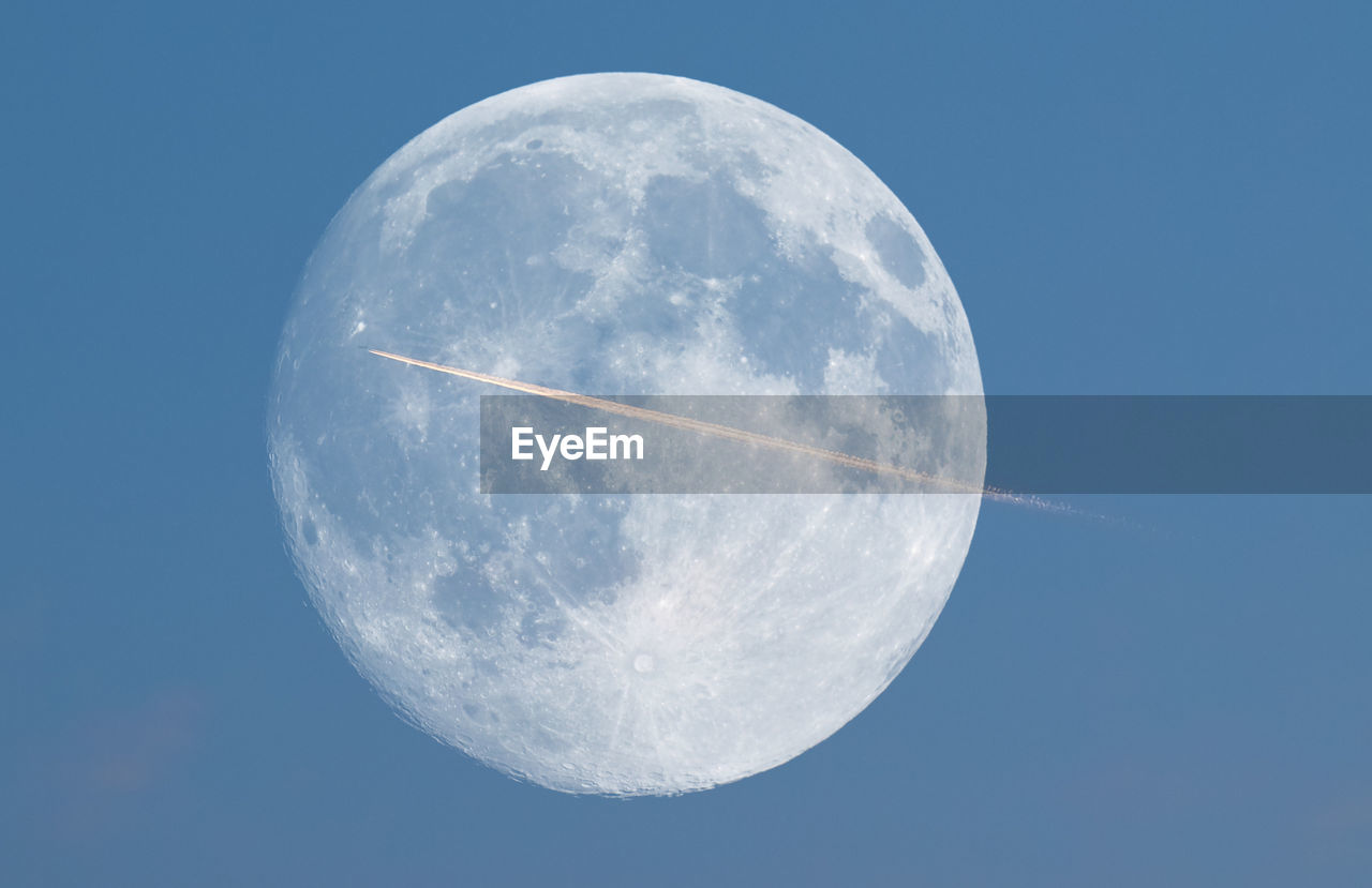 Low angle view of vapor trail against full moon at dusk