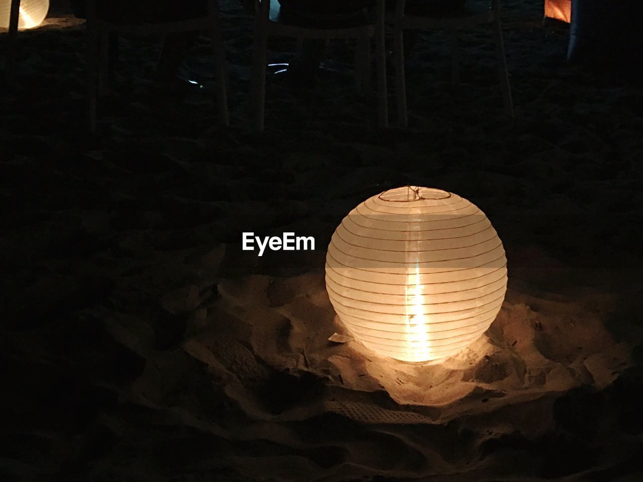 Illuminated paper lantern on sand at night