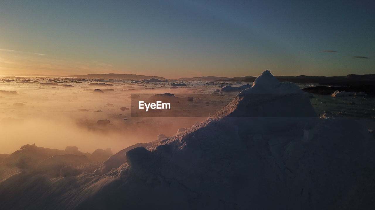 SNOW COVERED LANDSCAPE AGAINST SKY DURING SUNSET