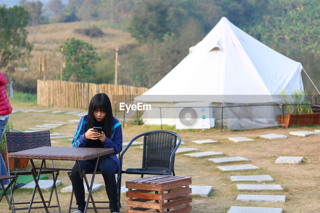Young woman using smart phone while sitting on chair at campsite