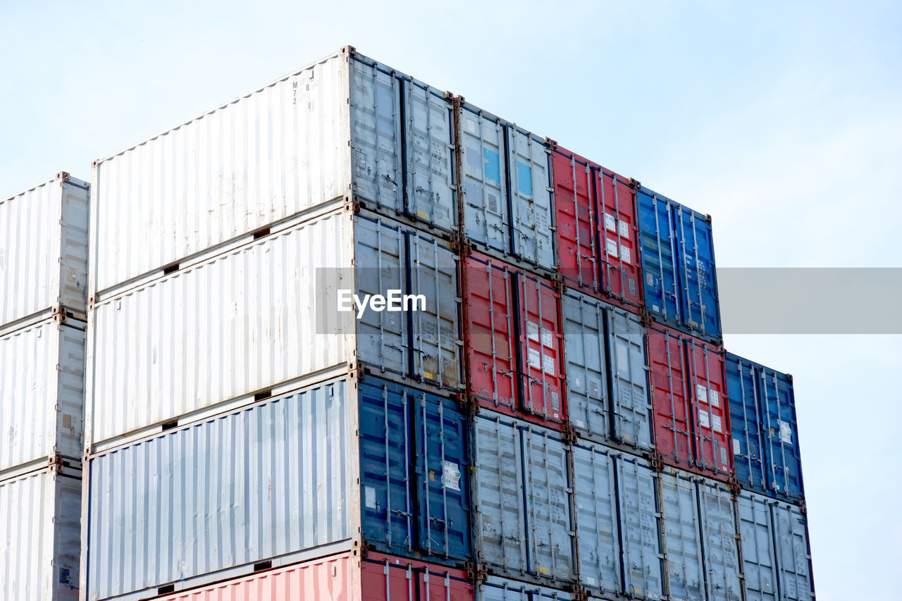 Low angle view of cargo containers stack against sky