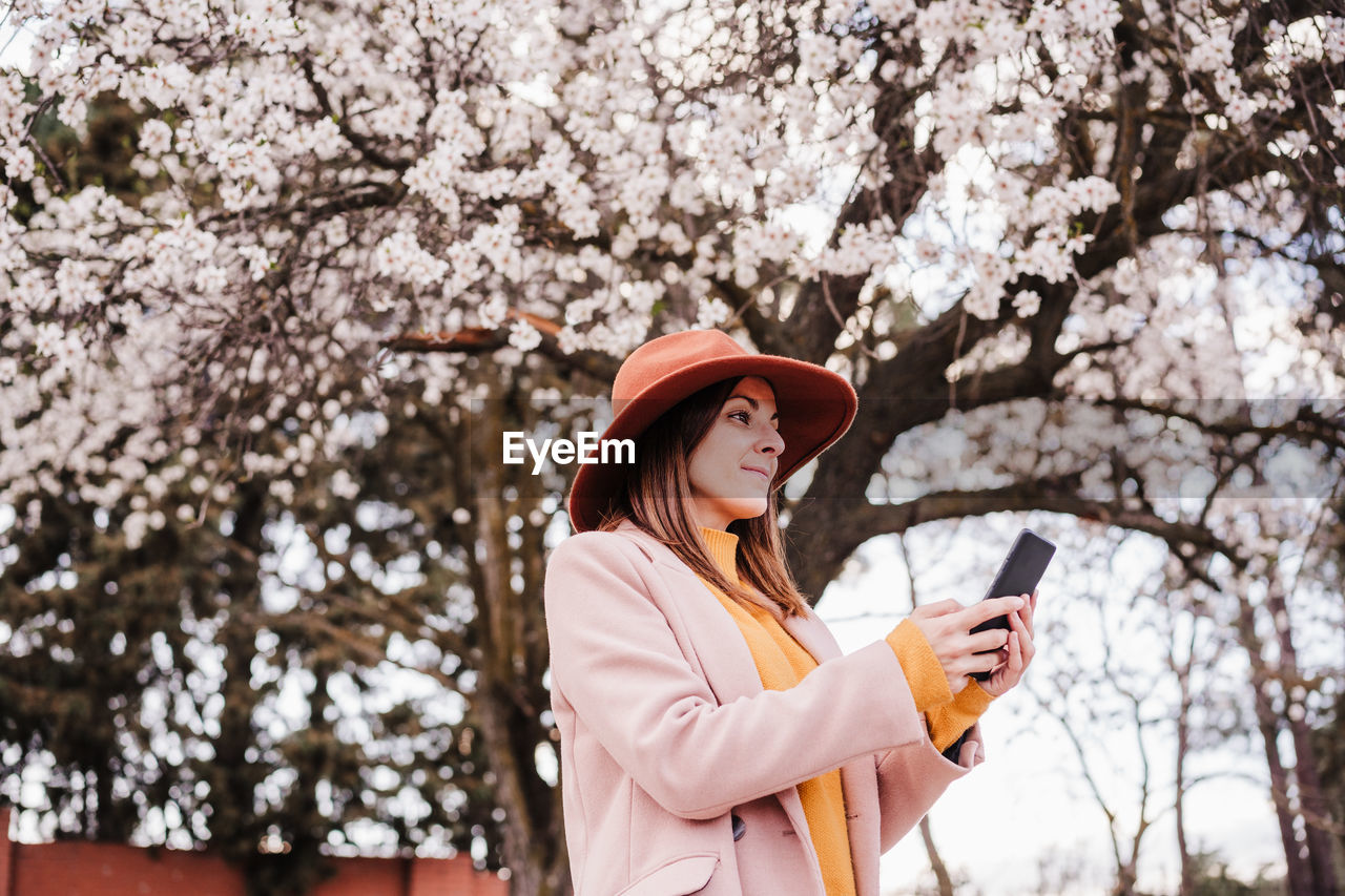 Low angle view of woman wearing hat against cherry blossom