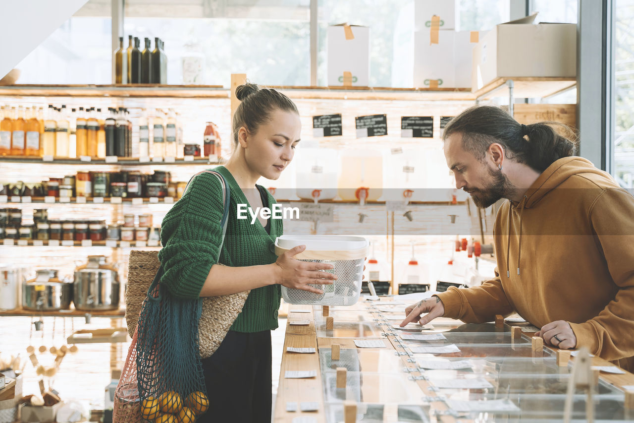 Man reading labels on counter by woman with container in shop